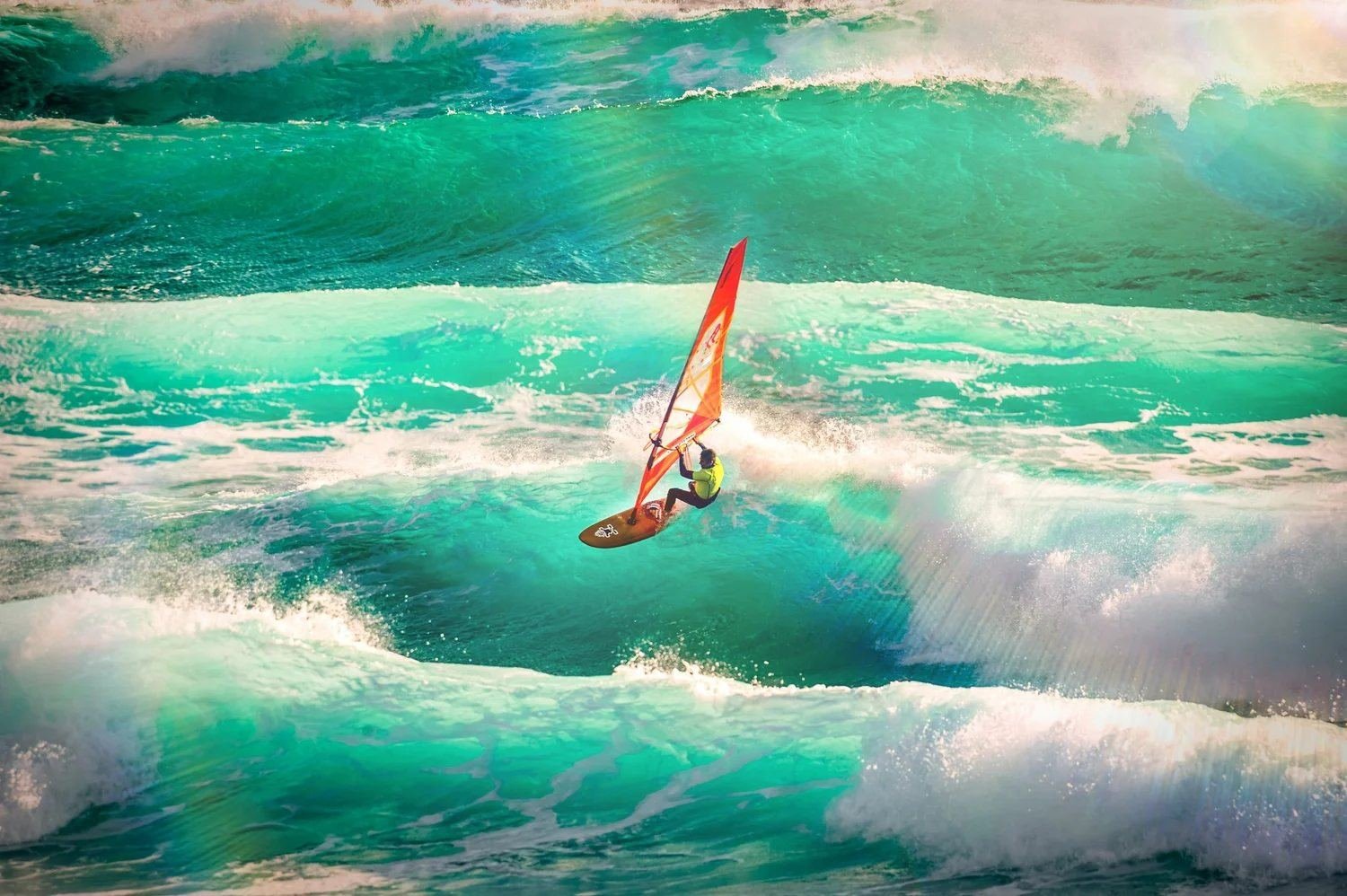 A windsurfer with an orange sail rides a teal Atlantic wave
